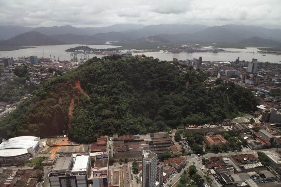 Região montanhosa de Santos mostra morro cercado por moradias e prédios.