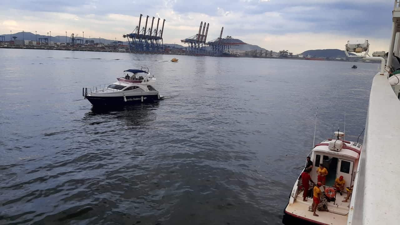 Lancha usada na operação se aproxima do navio. Ao fundo é possível ver o porto de santos.