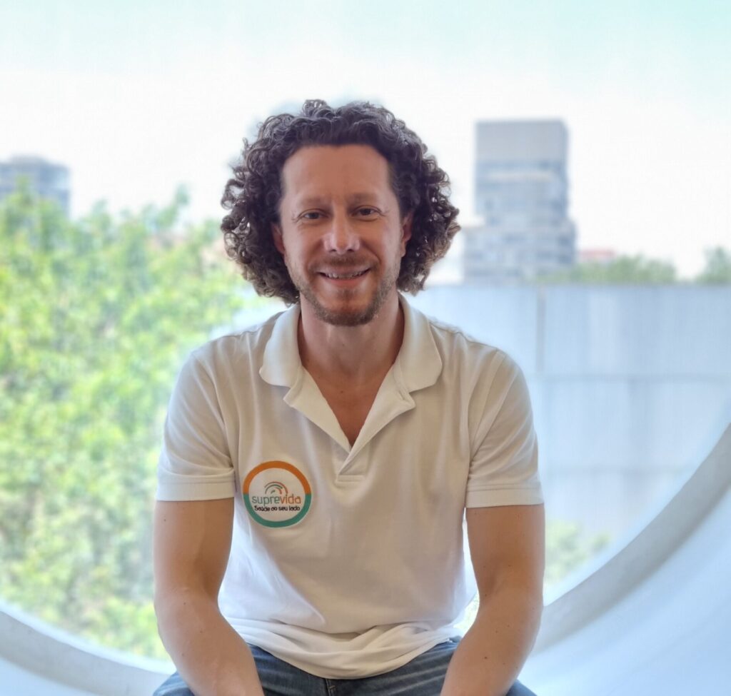 Rodrigo Correia da Silva é um homem branco, de cabelo cacheado longo, com cavanhaque. Veste camisa tipo polo que tem a logomarca da empresa na lapela direita. Esta sentado tendo uma janela arredondada atrás, onde é possível ver uma árvore e parte de um prédio.