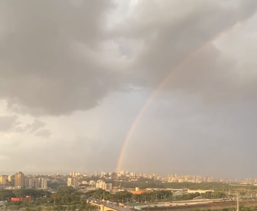 Imagem panorâmica da cidade de São Paulo mostra arco-ires sobre a Marginal Tietê. O céu encoberto por nuvens e um tom rosa sobre a cidade.