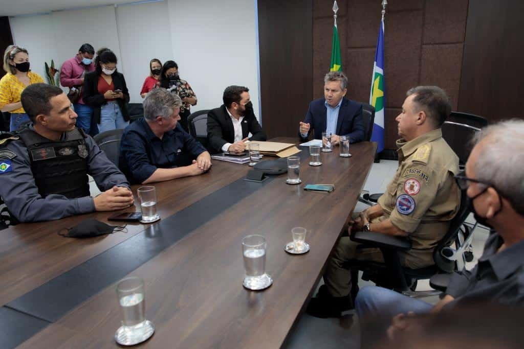 Governador Mauro Mendes, homem de pele branca e cabelos grisalhos, sentado à mesa, conversa com integrantes do governo e comando das polícias. 