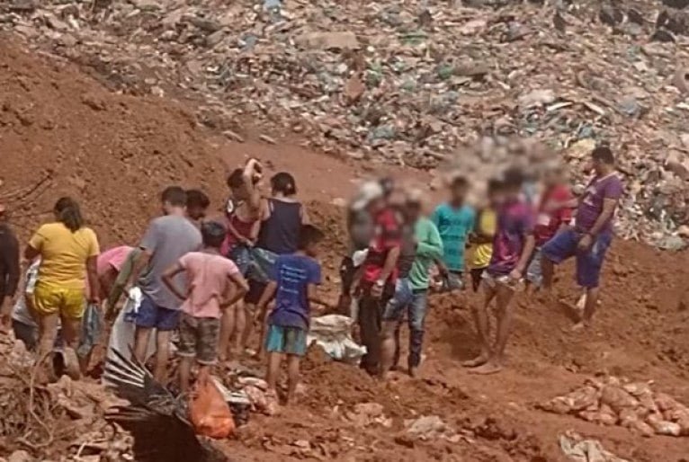 Fila de pessoas na base de uma montanha de lixo procuram por alimentos.