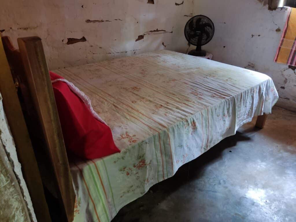 Foto mostra quarto em que a criança foi morta. O cômodo tem um ventilador giratório perto da parede, uma cama de casal, onde mãe e filho se esconderam dos criminosos. 