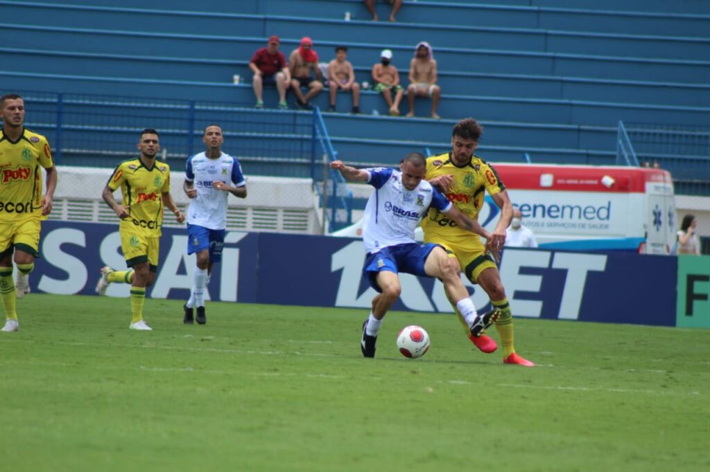 Jogador do Mirassol tenta tirar a bola dos pés de jogador do Santo André disputam a bola enquanto outros atletas acompanham ao fundo