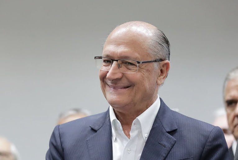 Geraldo Alckmin, homem de pele clara, usa óculos de grau com armação discreta. Calvo, tem cabelos grisalhos na lateral da cabeça. 