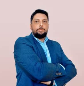 Felipe Locato, homem de pele morena, aparece de paletó com os braços cruzados.