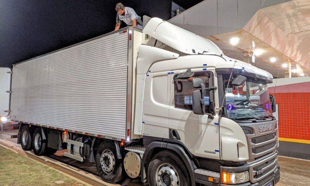 Caminhão alvo de buscas por policiais durante investigação. Policial aparece em cima do baú.