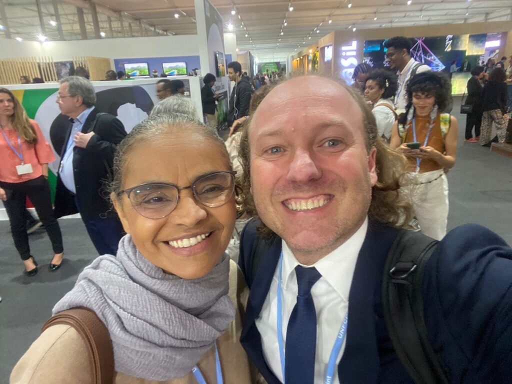 Rodrigo Agostinho, homem de pele clara, cabelos compridos em cachos, sorri pra foto ao lado de Marina Silva, ministra do meio ambiente.