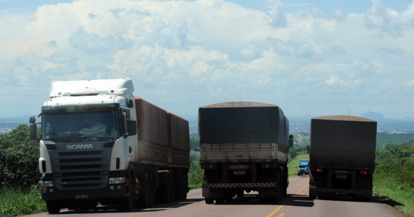 Três caminhões aparecem lado a lado na rodovia, enquanto um está de frente para foto e outros dois em sentido contrário.