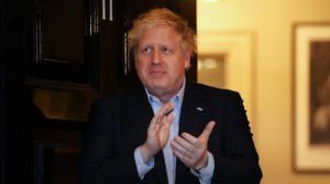 Boris Johnson, ex-primeiro ministro britânico, bate palmas enquanto olha para o lado.