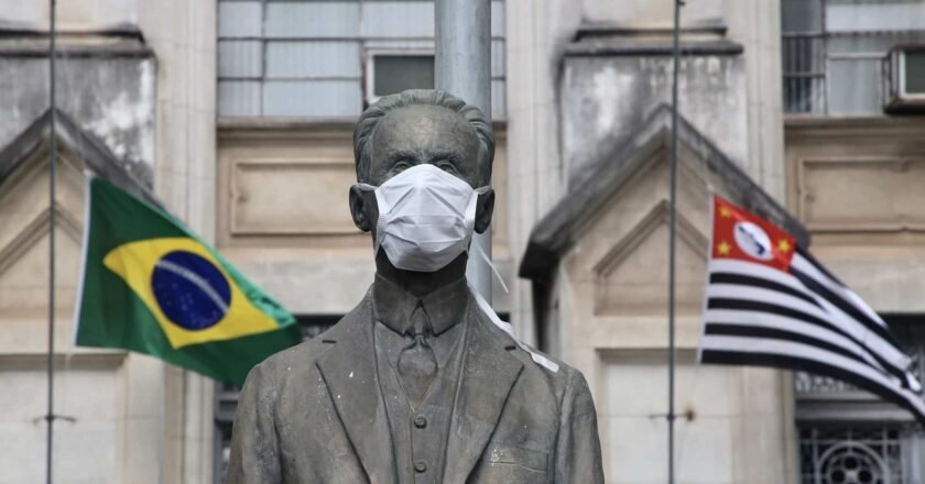 Fachada do Instituto Butantan com estátua usando máscara, tendo atrás as bandeiras do Brasil e do Estado de São Paulo