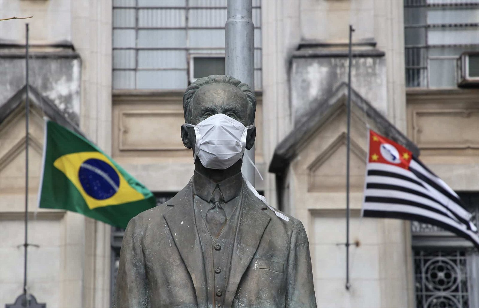 Fachada do Instituto Butantan com estátua usando máscara, tendo atrás as bandeiras do Brasil e do Estado de São Paulo