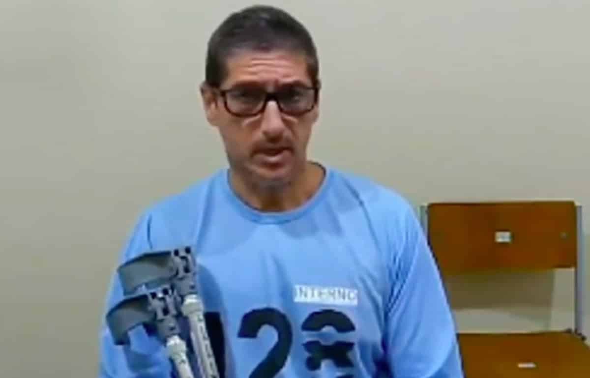 Ronnie Lessa, de camiseta azul, segurando muletas. É um homem de cor de pele clara, óculos de grau.