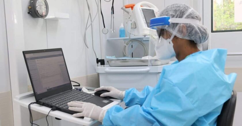 Cientista em laboratório da Fiocruz, usando equipamentos de proteção individual no corpo e na cabeça, além de luvas, utiliza computador dentro do laboratório.