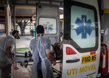 Paciente é colocado em ambulância por dois socorristas que usam equipamentos de proteção pessoal
