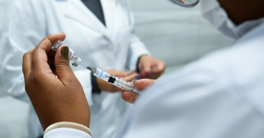 agente de saúde prepara a vacina removendo o imunizante do frasco com um seringa