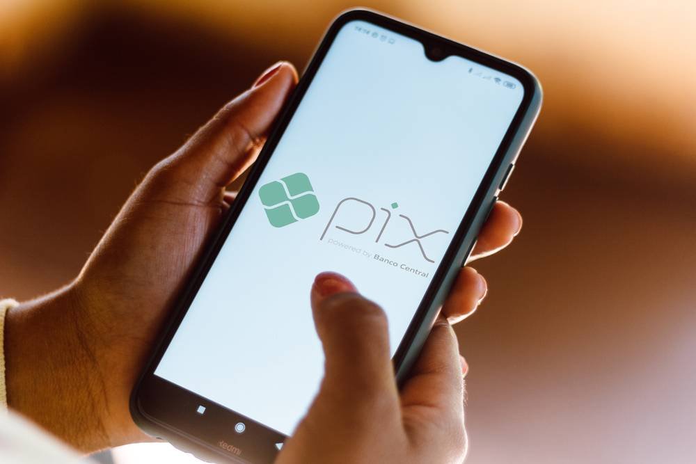 Mãos seguram celular que tem na tela a imagem do PIX 