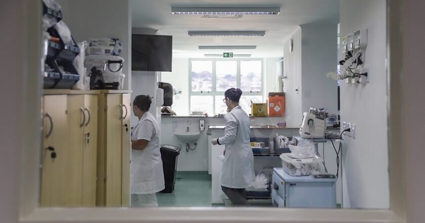 enfermeiras trabalham dentro de uma sala do hospital. Foto mostra o balcao de atendimento no primeiro plano e equipamentos próximo de duas profissionais de saúde.