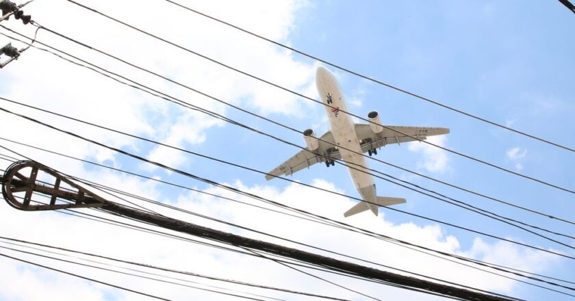 Avião sobrevoa bairro em São Paulo . No primeiro plano aparecem fios da rede elétrica.