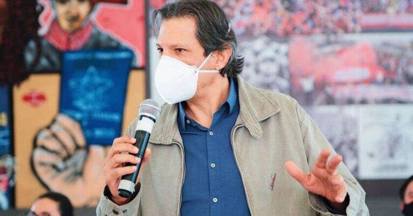 Fernando Haddad, ex-ministro da educação, de máscara, com microfone na mão, durante palestra
