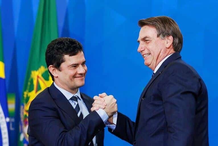 Sergio Moro e Jair Bolsonaro se cumprimentam enquanto sorriem