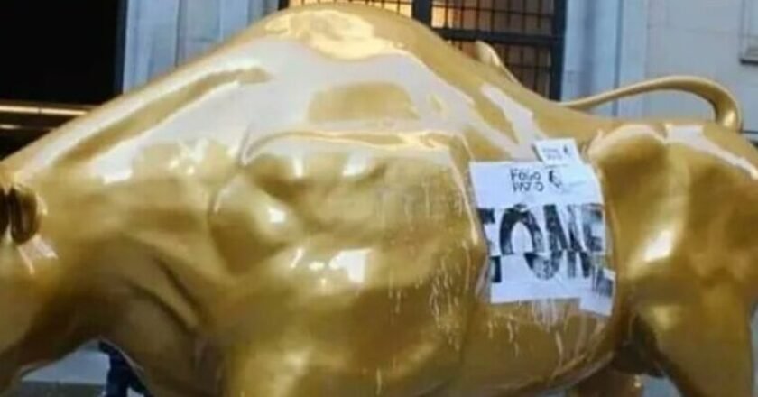 Touro de ouro em frente ao prédio da Bolsa de Valores com cartaz colado. Palavra fome escrita no cartaz.
