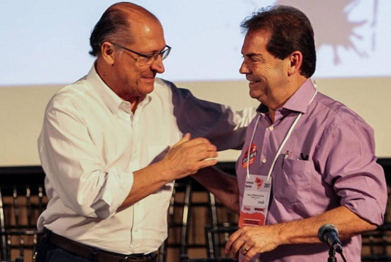 Geraldo Alckmin cumprimenta Paulinho da força. Alckmin veste camisa social azul clara e Paulinho está de camisa social vinho, com crachá.