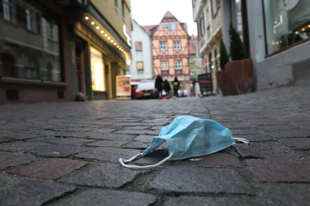 Máscara caída no chão em calçamento de uma rua da alemanha. Ao fundo, pessoas caminhando.