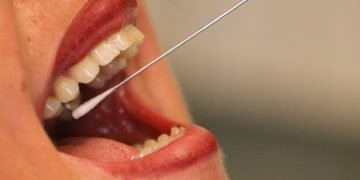 Foto em close na boca aberta de uma pessoa e haste de coleta de pcr dentro da boca.