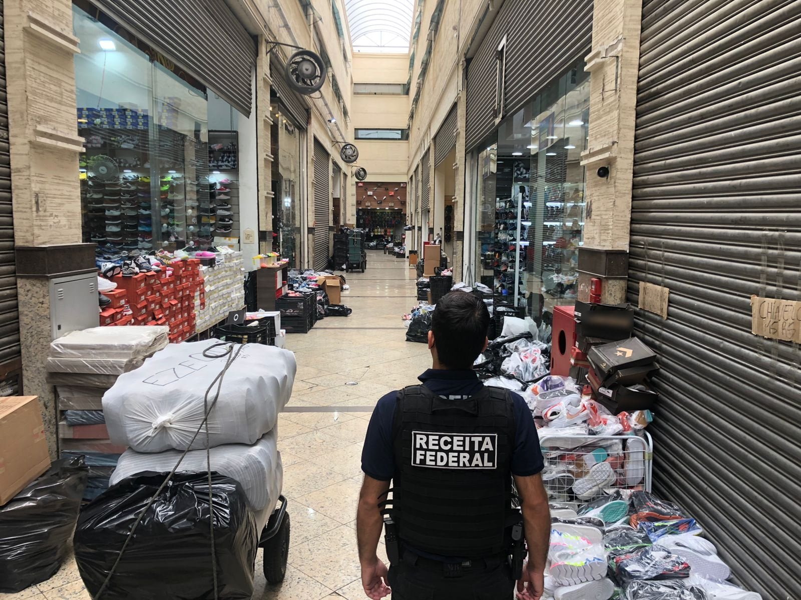 Agente da receita federal, no meio do corredor de um shopping popular, com mercadorias encostadas nas paredes
