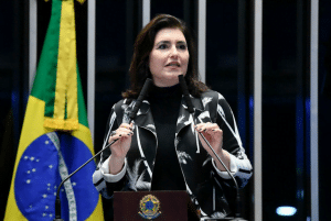 Senador Simone Tebet, com blusa estampada em preto e branco, discursa na tribuna. Ao fundo, parte da bandeira do Brasil.