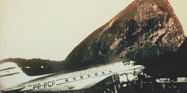 Avião antigo estacionado no Rio de Janeiro, com o Pão de Açúcar ao fundo.