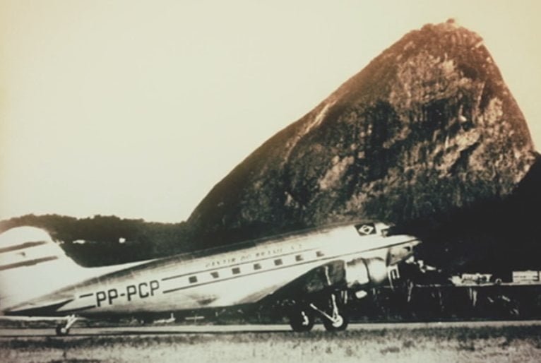 Avião antigo estacionado no Rio de Janeiro, com o Pão de Açúcar ao fundo.