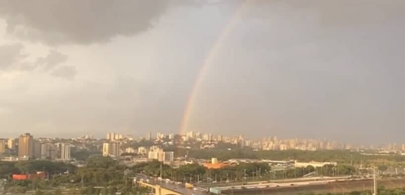 Imagem panorâmica da cidade de São Paulo mostra arco-ires sobre a Marginal Tietê. O céu encoberto por nuvens e um tom rosa sobre a cidade.