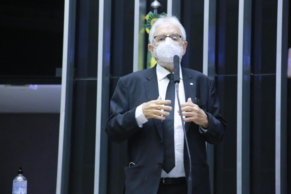Ivan Valente, homem de pele branca, cabelos brancos, usa óculos e máscara de proteção enquanto discursa em tribuna da Câmara dos Deputados. 