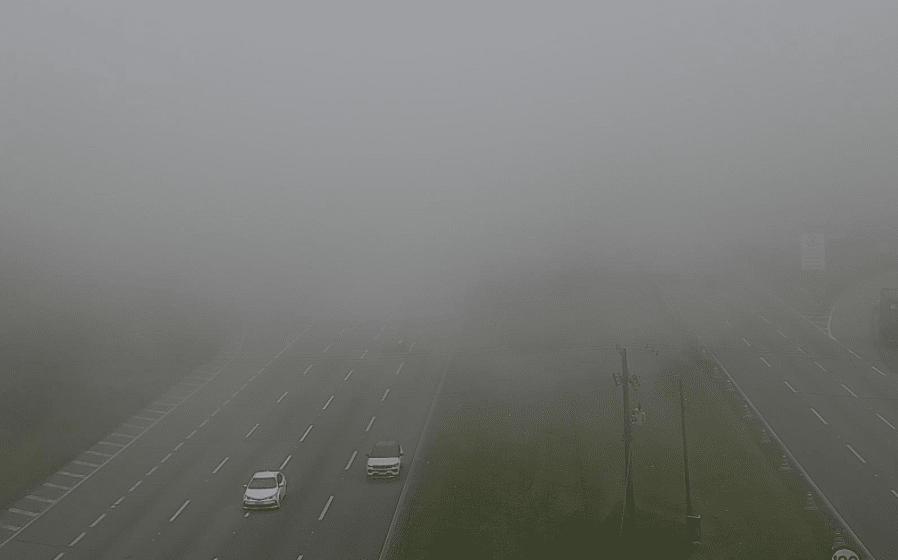 Foto mostra carros saindo do meio da neblina e fumaça impedindo visibilidade mais distante, cobrindo as duas pistas. 
