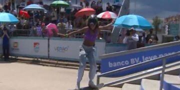 Rayssa Leal faz uma manobra aérea com skate, deslizando sobre barra de ferro . Ao fundo, público acompanha debaixo de guarda-sois coloridos.