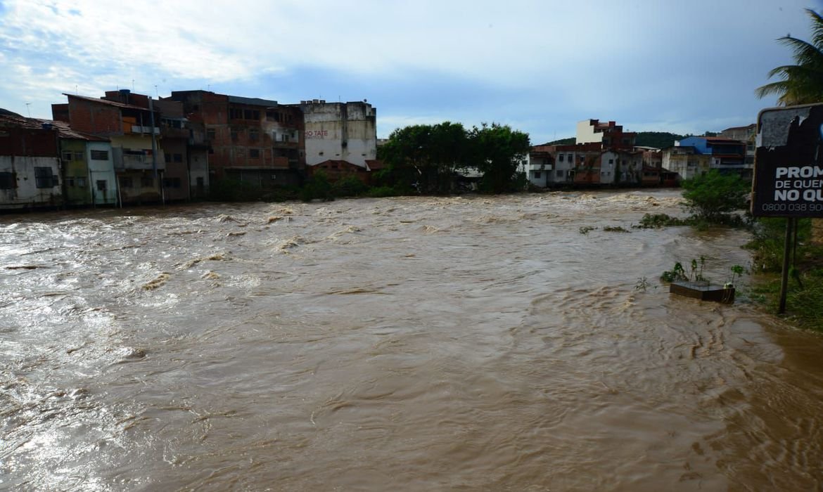 Imagem mostra nível do rio elevado com casas ao fundo bem perto da lâmina d'água