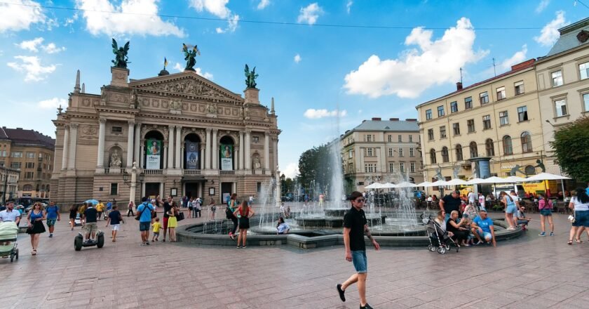 Fachada do teatro ópera e balé diante da praça onde é possível ver uma fonte lançando água para o alto e pessoas caminhando pela praça em Lviv, na Ucrânia.