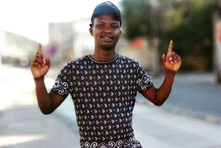 Moïse Kabagambe, jovem negro, vestindo camiseta e boné. Sorri para foto com os dois dedos indicadores apontados par ao céu.