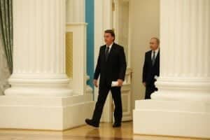 Entre dois grandes pilares, na parte interna do palácio, Jair Bolsonaro caminha à frente de Vladimir Putin.