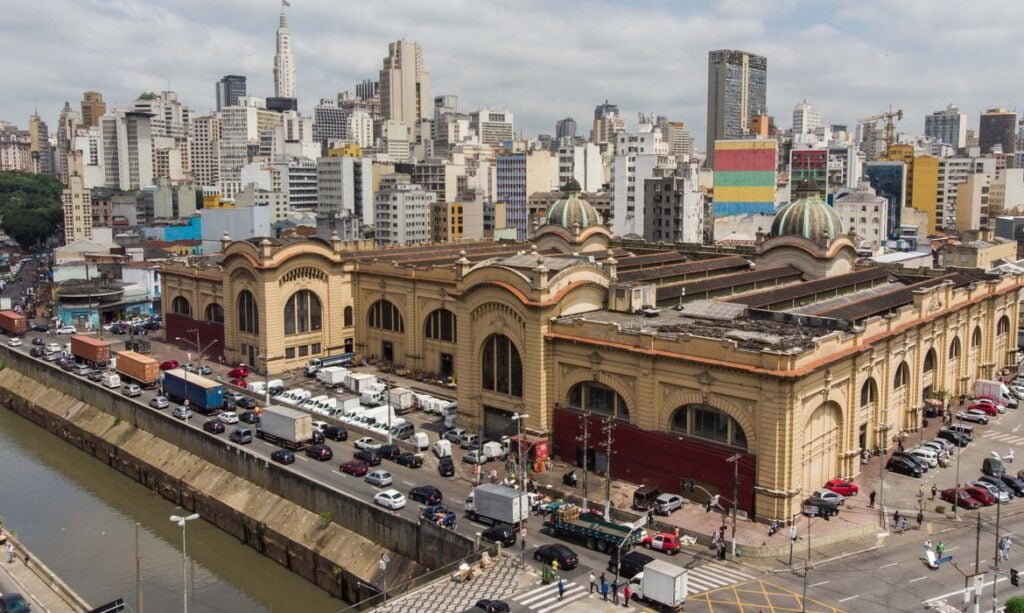 Imagem panorâmica mostra mercadão municipal de São Paulo. Do lado esquerdo é possível ver o rio Tamanduateí e carros passando pela Avenida do Estado.