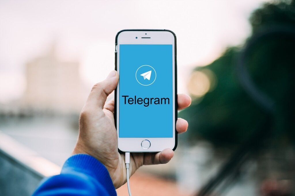 Mão segurando o celular no alto, com a tela aberta na pagina inicial do Telegram.