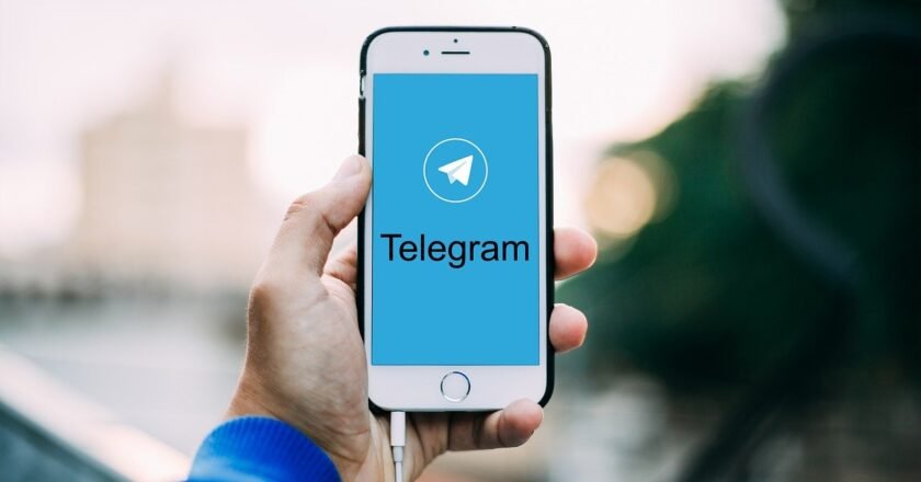 Mão segurando o celular no alto, com a tela aberta na pagina inicial do Telegram.