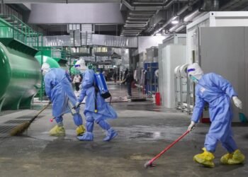 Com roupas de proteção e vassouras, trabalhadores limpam local onde funciona maior hospital provisório de Xangai.