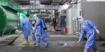 Com roupas de proteção e vassouras, trabalhadores limpam local onde funciona maior hospital provisório de Xangai.
