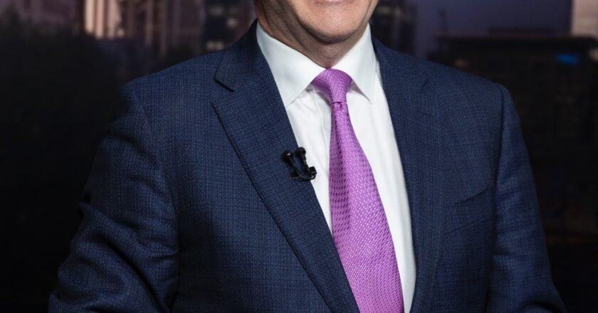 Anthony Albanese, homem de pele clara, óculos de grau arredondado, sorri enquanto concede entrevista em um estúdio, vestindo terno e gravata.