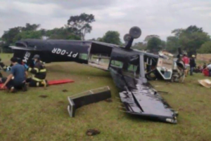 Avião com as rodas para cima e socorristas atendendo vítimas no gramado ao lado