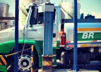 Caminhão que transporta combustível estacionado diante de tanques de armazenamento de combustível. Na lataria do caminhão é possível ver a marca da Petrobras: "BR".