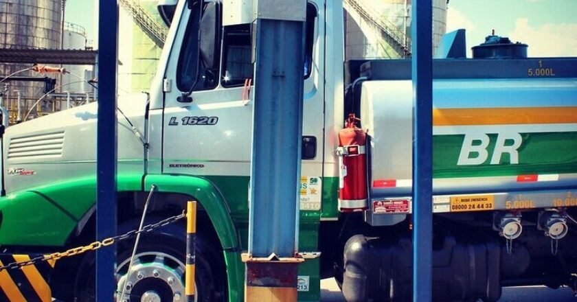 Caminhão que transporta combustível estacionado diante de tanques de armazenamento de combustível. Na lataria do caminhão é possível ver a marca da Petrobras: "BR".